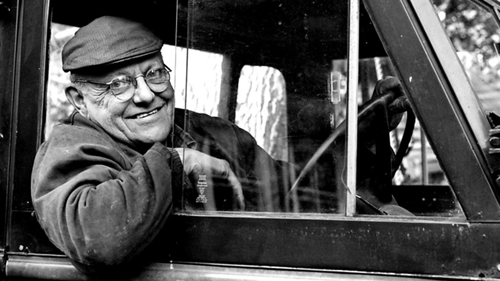Old man looking out from vintage car window smiling