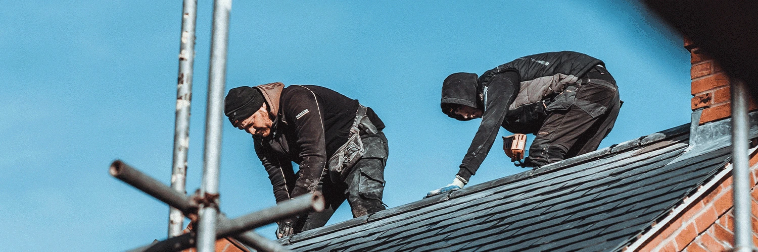 two roofers working on the roof replacing tiles